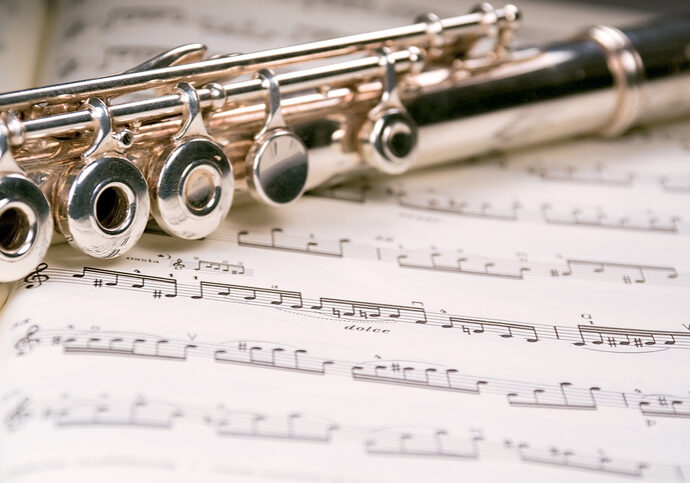 A used flute rests across an open musical score. Only one line of music is in focus.