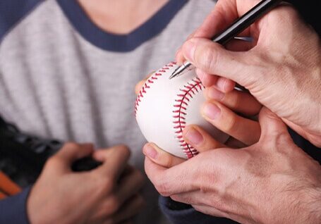 Man signing autograph on baseball for child fan
