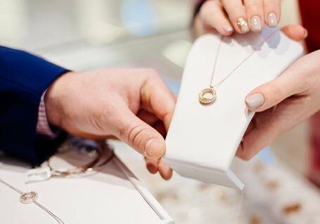 Man being helped at jewelry counter, looking at necklace with employee